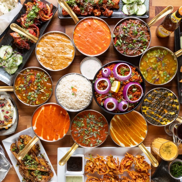 A vibrant spread of Indian dishes, including curries, rice, and appetizers, on a wooden table.