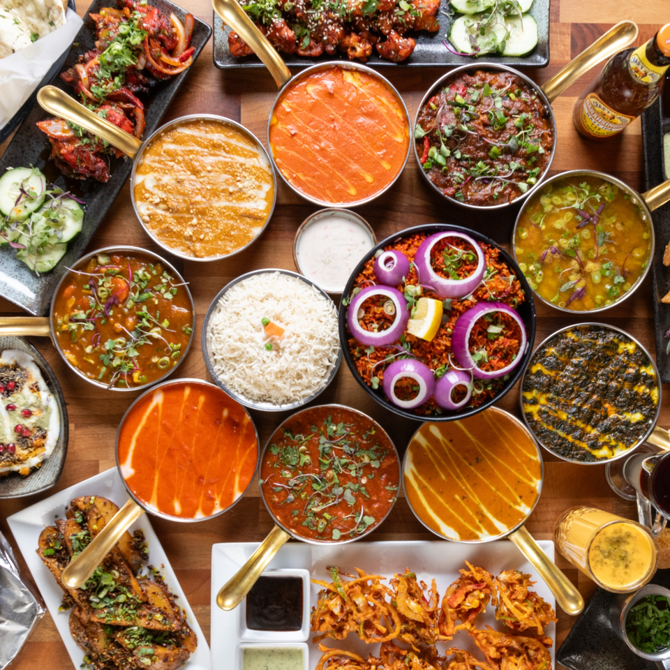 A vibrant spread of Indian dishes, including curries, rice, and appetizers, on a wooden table.