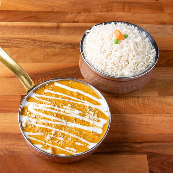 Creamy orange curry with white drizzle and rice with peas and carrots on a wooden table.