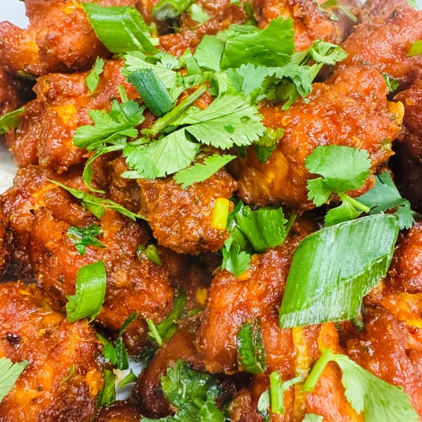 Close-up of vibrant orange Indian chicken dish, garnished with fresh green cilantro and scallions.