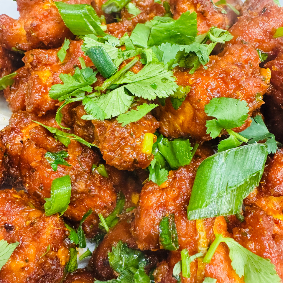 Close-up of vibrant orange Indian chicken dish, garnished with fresh green cilantro and scallions.