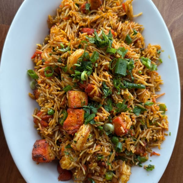 Close-up of Indian chicken biryani with rice, chicken, shrimp, and fresh herbs on a white plate.