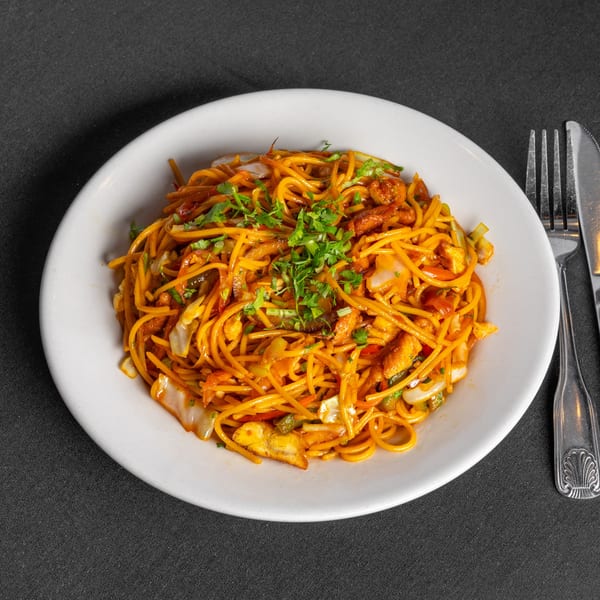 A white plate of Indian-style noodles with chicken, vegetables, and fresh cilantro on a dark tablecloth.