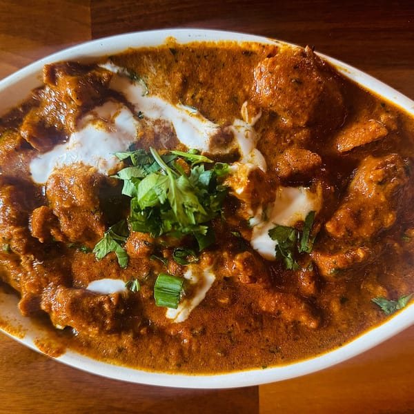 A close-up of Indian butter chicken, garnished with fresh cilantro and a swirl of cream.