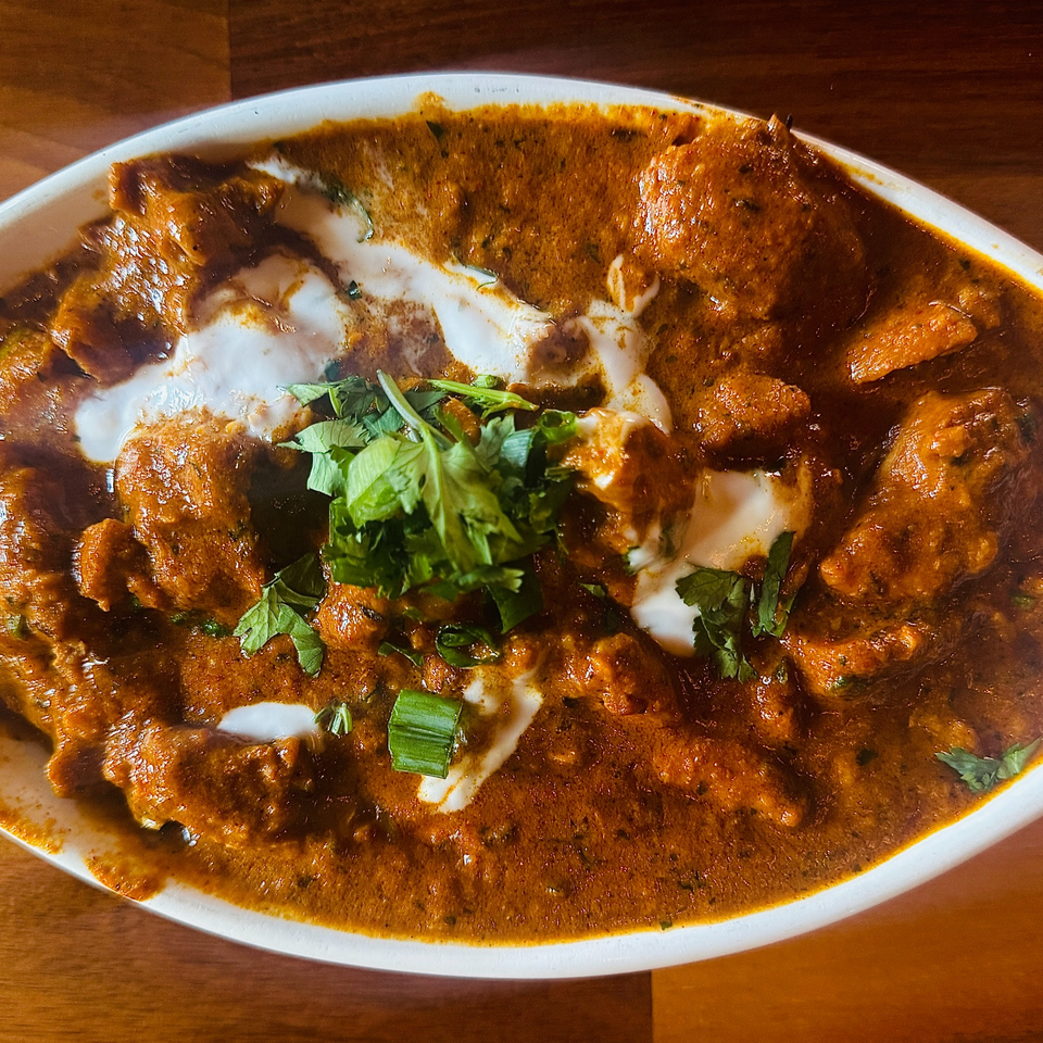 A close-up of Indian butter chicken, garnished with fresh cilantro and a swirl of cream.
