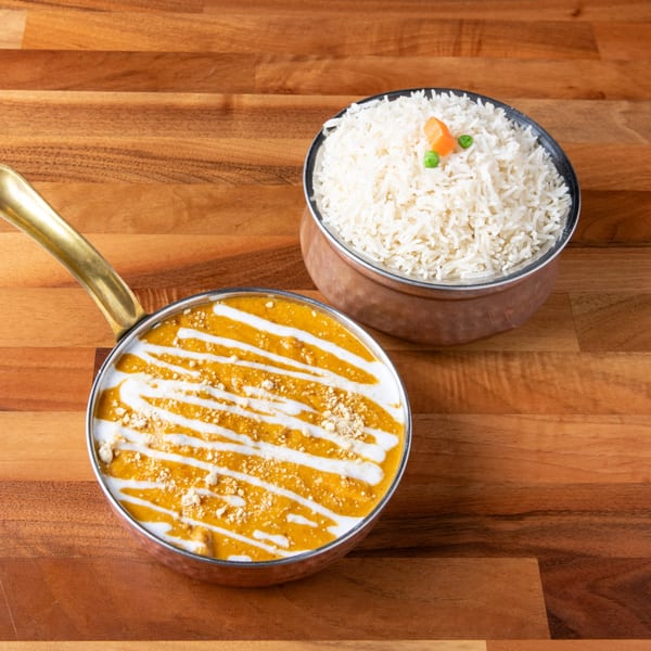 Creamy orange curry with white drizzle and rice with peas and carrots on a wooden table.