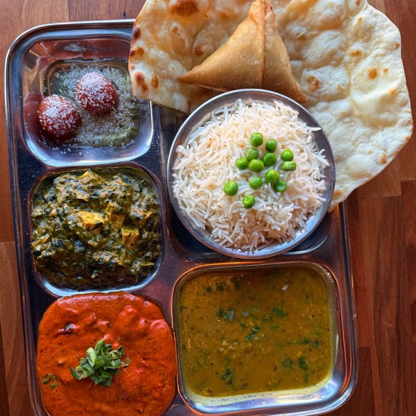 An Indian thali with palak paneer, butter chicken, dal, rice, gulab jamun, samosas, and naan.