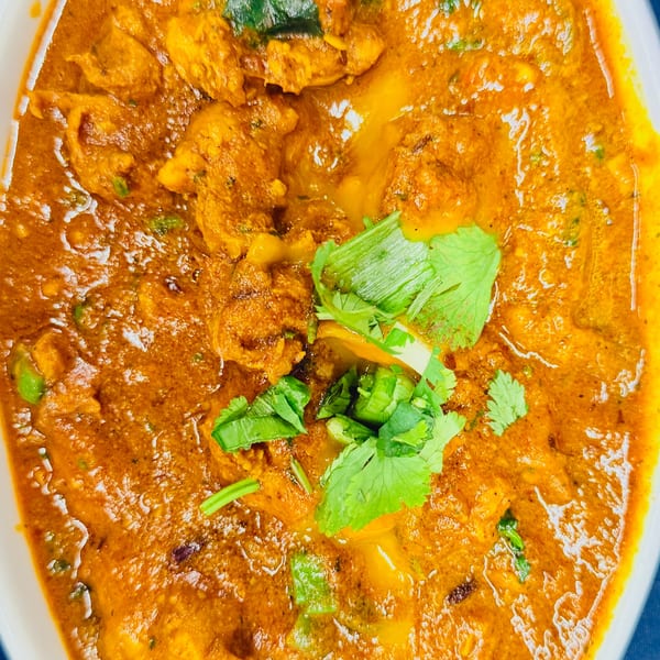 Close-up of a vibrant orange Indian curry with chicken pieces, garnished with fresh green cilantro.