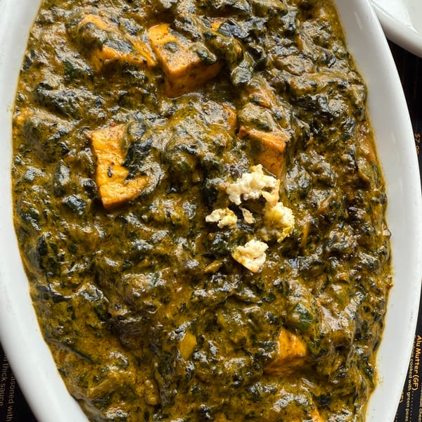 Close-up of Palak Paneer, a vibrant green Indian spinach and cheese curry, in a white dish.