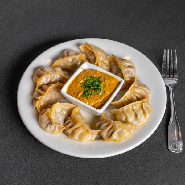 Plate of Indian momos, steamed dumplings, with a side of orange dipping sauce garnished with cilantro.