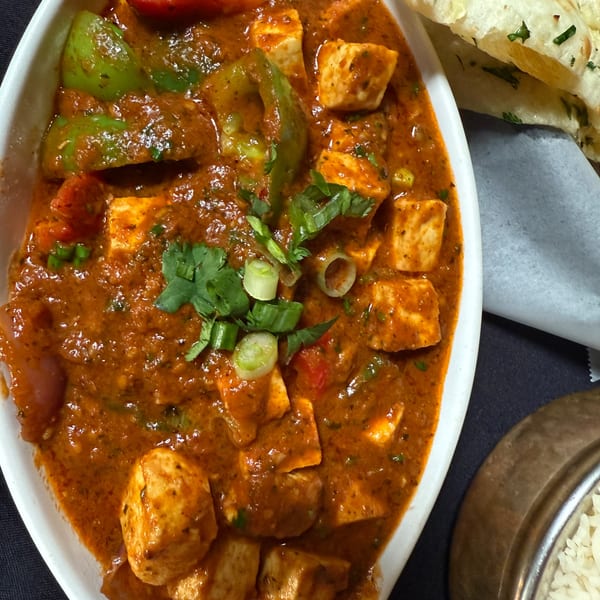 Close-up of Indian paneer curry with green peppers, garnished with cilantro and scallions, served with naan.