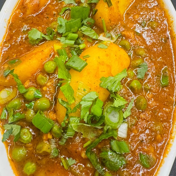 Aloo Matar, an Indian dish with potatoes and peas in a rich, orange-red curry sauce, garnished with fresh herbs.