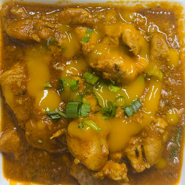 Close-up of a rich, orange Indian curry with chicken pieces, potatoes, and green garnishes.