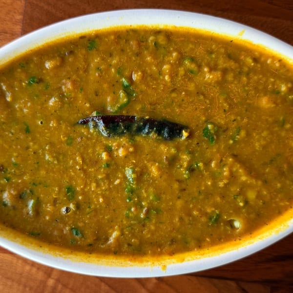 Close-up of Indian dal in a white oval dish, garnished with a dried red chili.