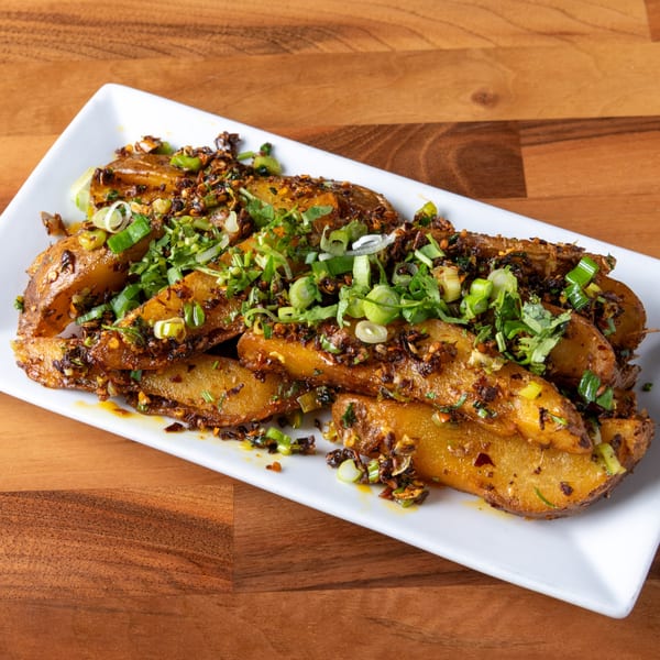 Crispy potato wedges topped with green onions, cilantro, and chili flakes on a white rectangular plate.