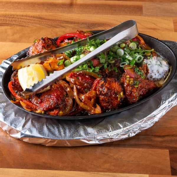 Sizzling chicken tikka masala with peppers, onions, cilantro, and lemon in a cast iron skillet.