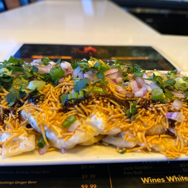 Close-up of Indian chaat with yogurt, chutney, sev, cilantro, and red onions on a white plate.
