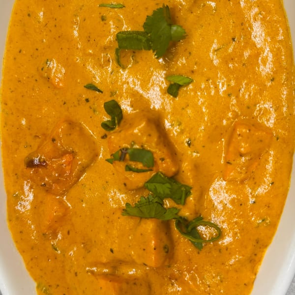 Close-up of Indian butter chicken, garnished with fresh cilantro, in a white bowl.