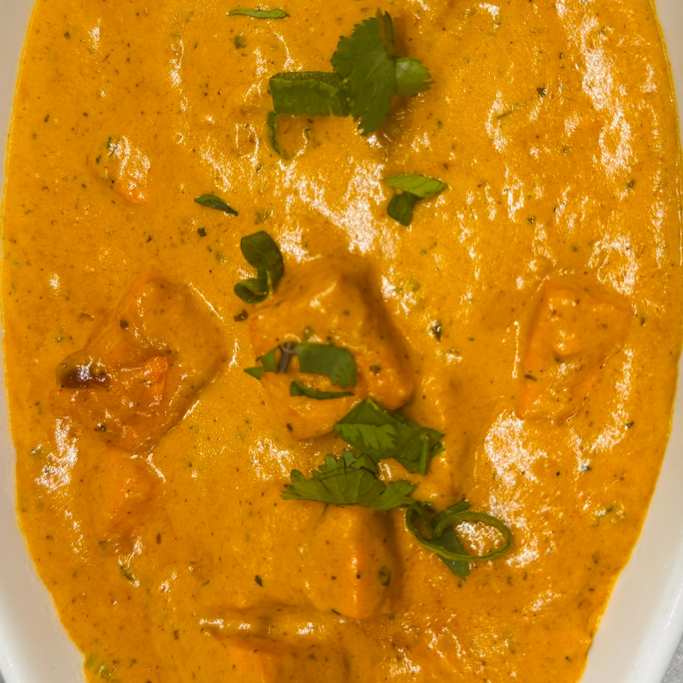 Close-up of Indian butter chicken, garnished with fresh cilantro, in a white bowl.