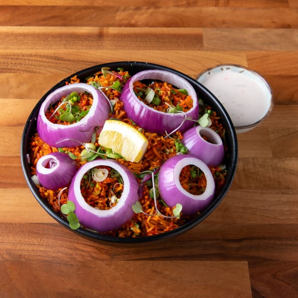 Spicy orange rice dish with red onion rings, lemon wedge, and microgreens, served with a side of white sauce.