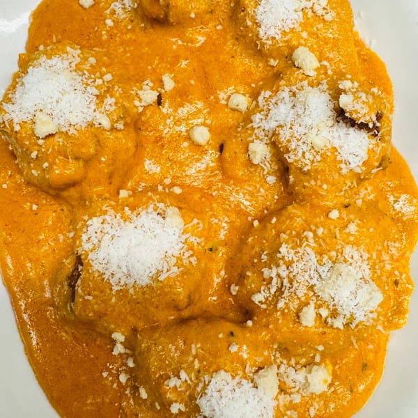 Close-up of Indian Malai Kofta, vegetable dumplings in a rich orange sauce, topped with shredded coconut.