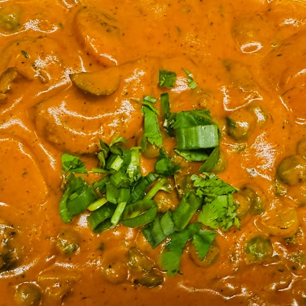 Close-up of Indian curry with a rich orange sauce, garnished with fresh green herbs.
