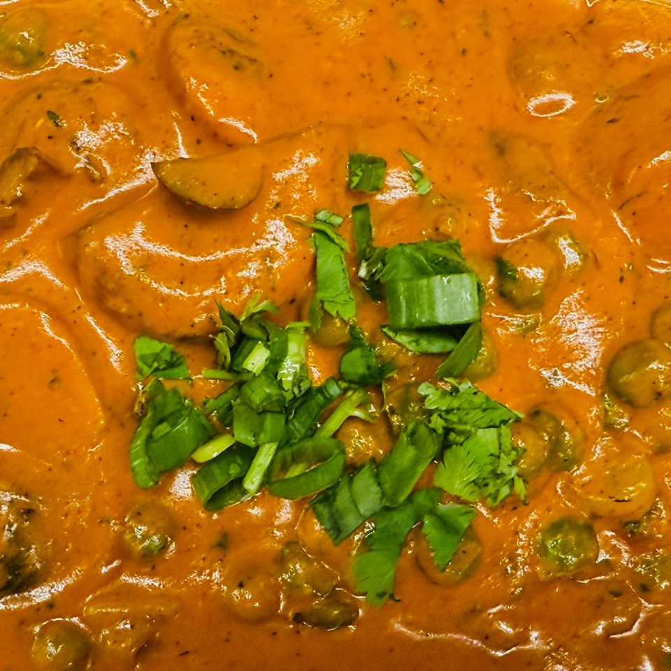 Close-up of Indian curry with a rich orange sauce, garnished with fresh green herbs.