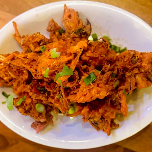 Close-up of crispy, orange Indian pakoras garnished with fresh green onions in a white bowl.