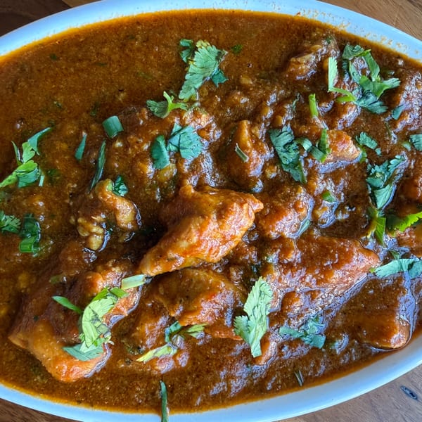 Close-up of Indian chicken curry with a rich, reddish-brown sauce and fresh green cilantro garnish.